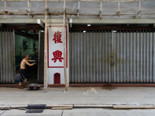 Free A man pushing a cart past a traditional Hong Kong storefront with bamboo scaffolding. Stock Photo