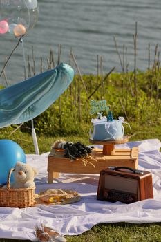 Charming outdoor birthday picnic setup by the water with cake, balloons, and gifts.