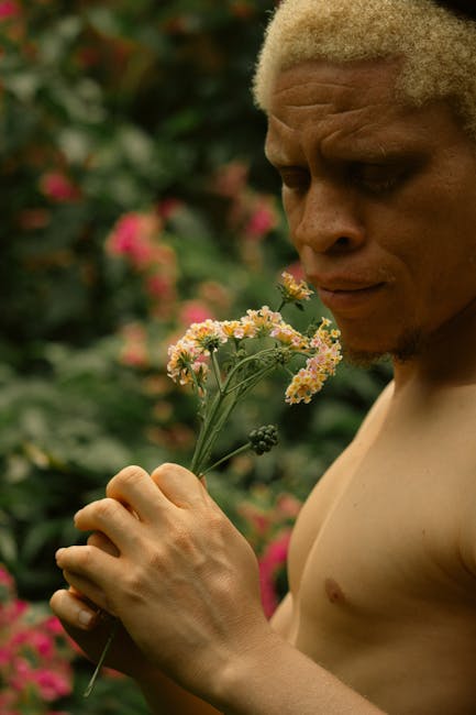 A man with albinism holding delicate flowers outdoors, surrounded by nature.