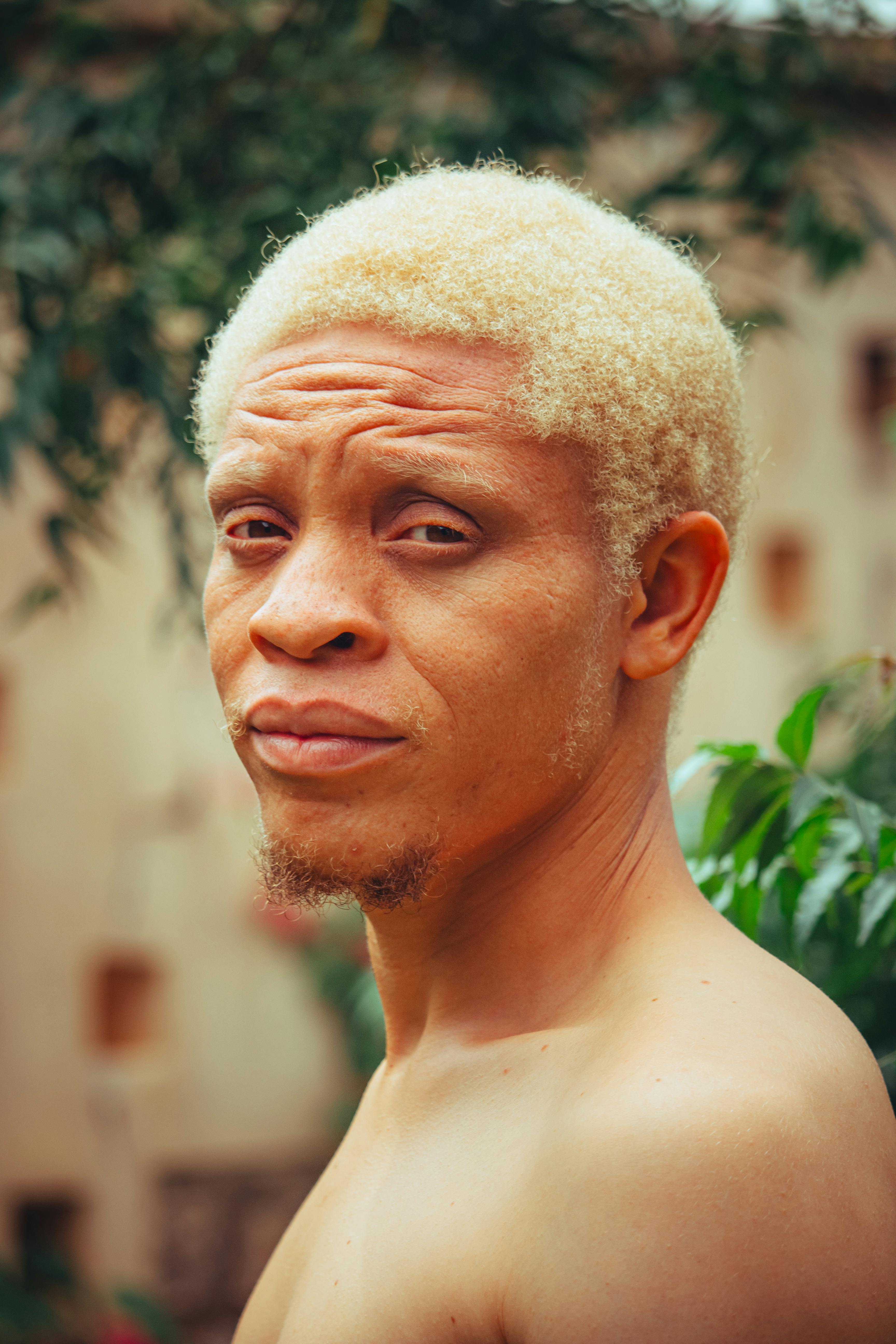 Close-up portrait of a man with blonde hair and neutral expression outdoors.