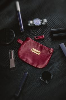 Stylish red leather pouch surrounded by accessories on a textured black surface.