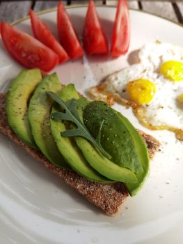 Healthy breakfast with avocado toast, eggs, and tomatoes on a sunny morning.