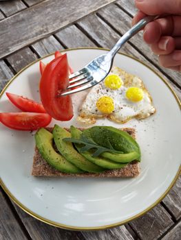 Plate with avocado toast, quail eggs, and sliced tomatoes on a wooden table.