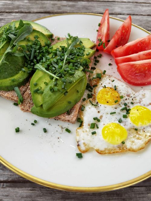 Free Delicious plate of avocado toast, cherry tomatoes, and sunny side up eggs garnished with chives. Stock Photo