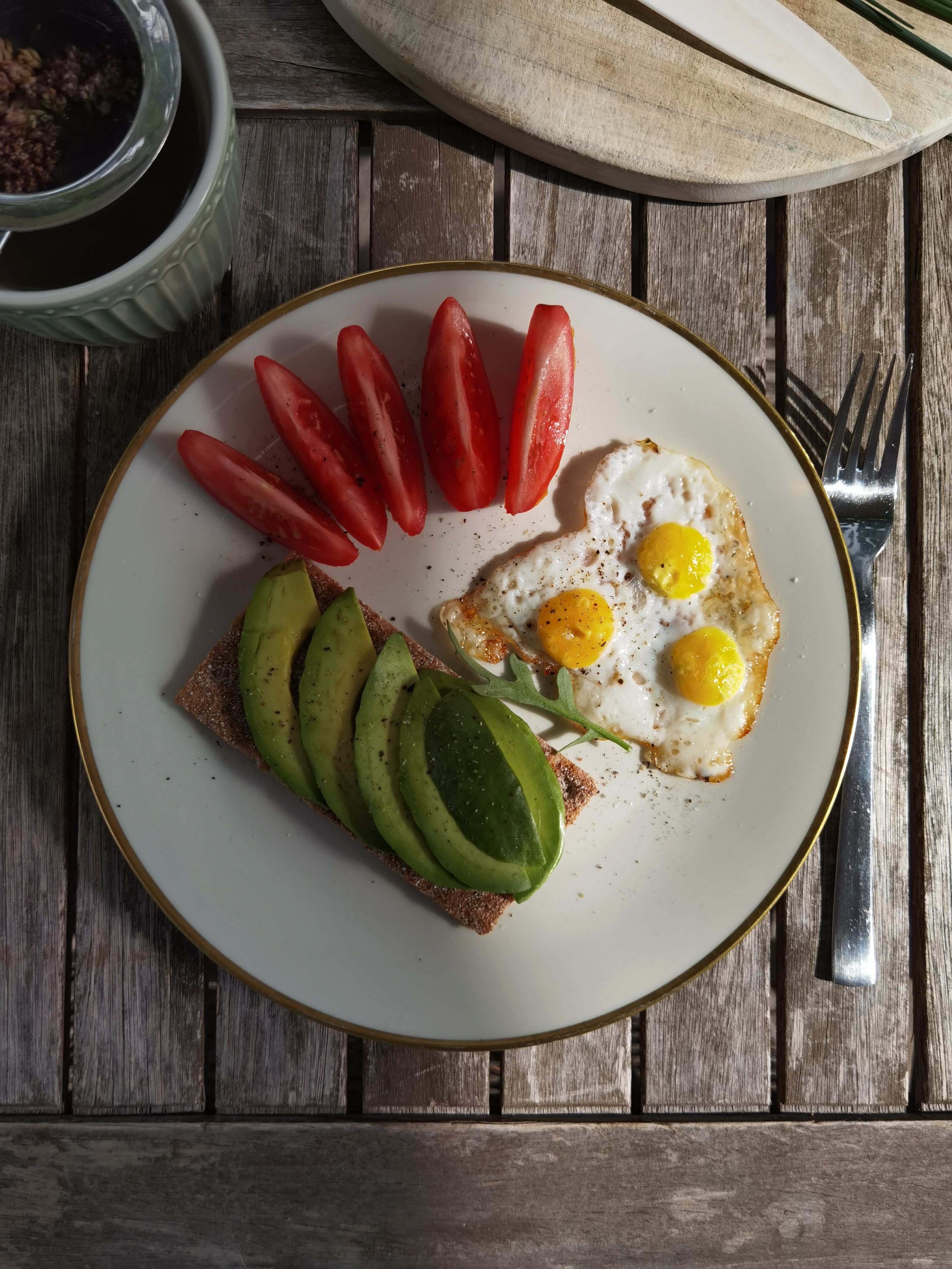 Delicious breakfast plate with avocado toast, quail eggs, and tomatoes on rustic table setting.