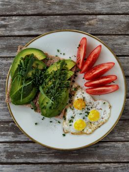 Tasty avocado toast served with fresh quail eggs and sliced tomatoes on a rustic table setting.