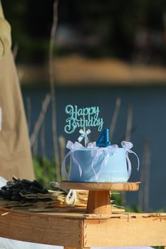 A charming blue birthday cake with candles and decor set outdoors by a lake.