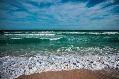 Free Captivating ocean waves breaking on a sandy beach under a bright blue sky. Stock Photo