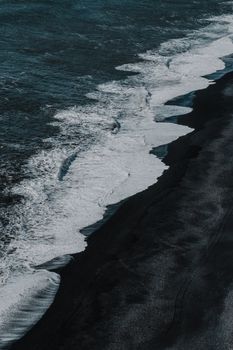 Aerial view of white foam waves against a striking black sand beach, offering a dramatic contrast.