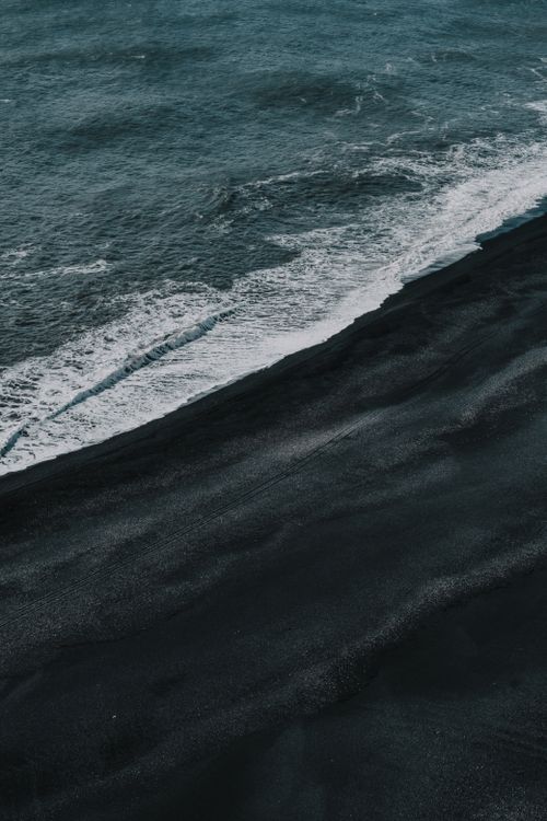 Free A striking view of ocean waves hitting a black sand beach, creating a dramatic landscape. Stock Photo