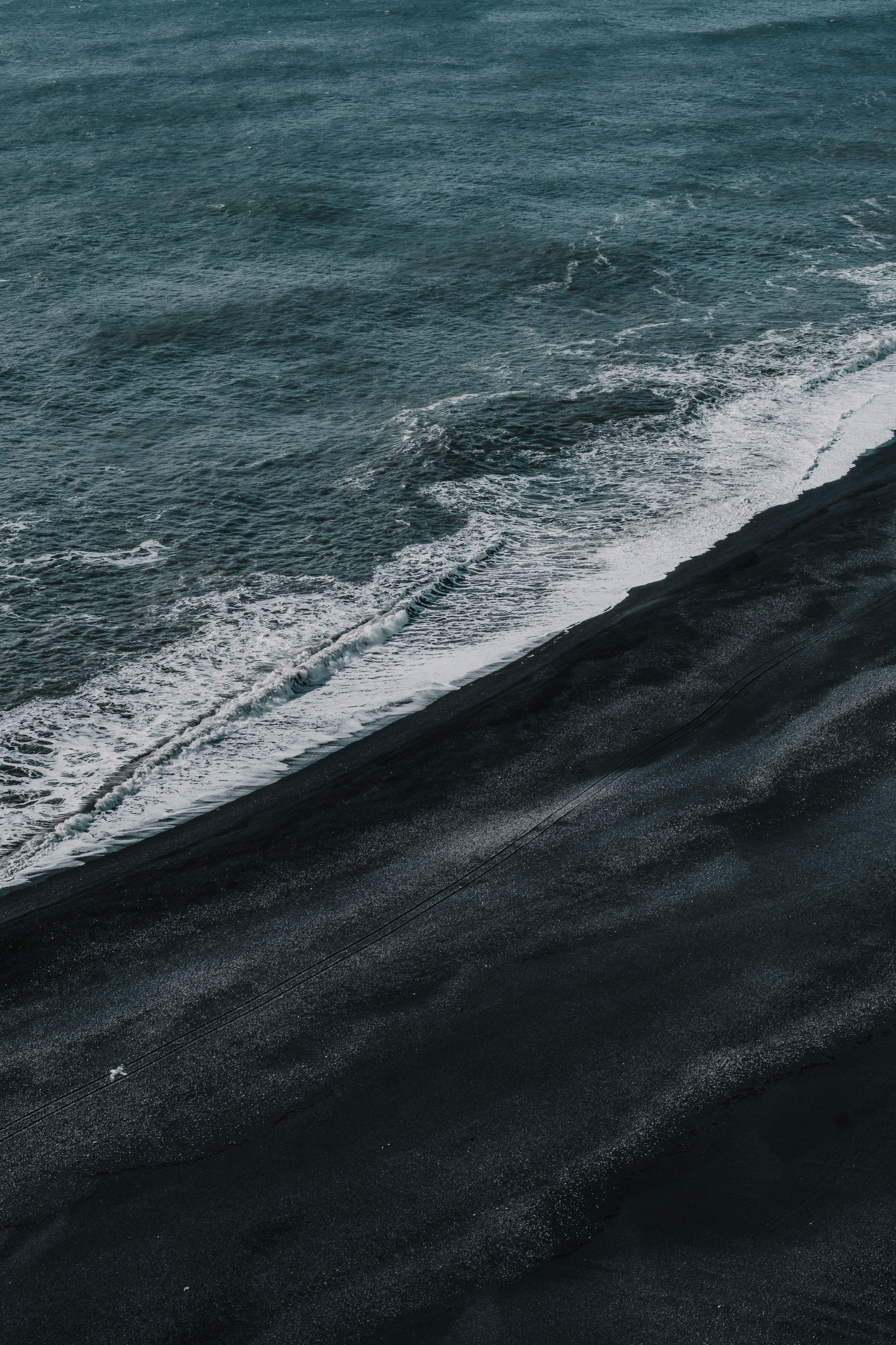Stunning aerial shot of a black sand beach meeting the ocean waves, creating a dramatic contrast.. pexels, stunning, aerial