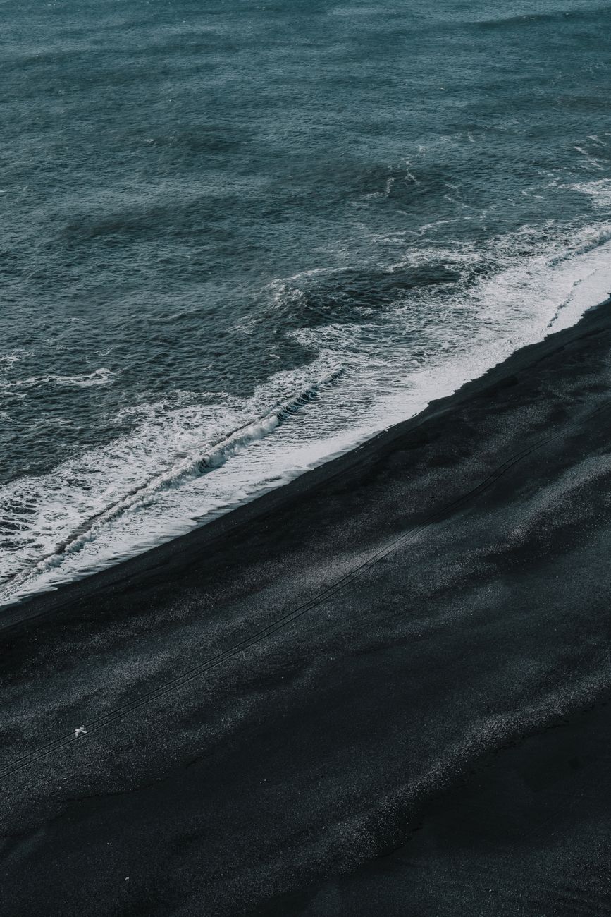 Stunning aerial shot of a black sand beach meeting the ocean waves, creating a dramatic contrast.. pexels, stunning, aerial