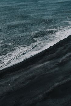 Stunning aerial shot of a black sand beach meeting the ocean waves, creating a dramatic contrast.. pexels, stunning, aerial