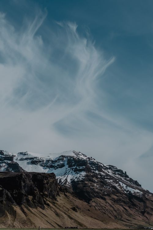 Free Snow-capped mountain peak with dramatic clouds and clear blue sky, showcasing nature's majesty. Stock Photo