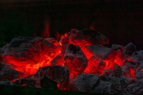 Free Close-up of glowing red hot coals in a dark fire pit, radiating intense heat. Stock Photo