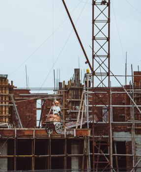 A construction worker on a scaffold at a building site with cranes and brickwork visible.