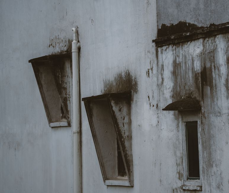 Weathered Mediterranean building facade with dark damp staining and peeling render around windows