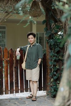 Woman in casual wear standing by a wooden garden gate outdoors, exuding a relaxed vibe.