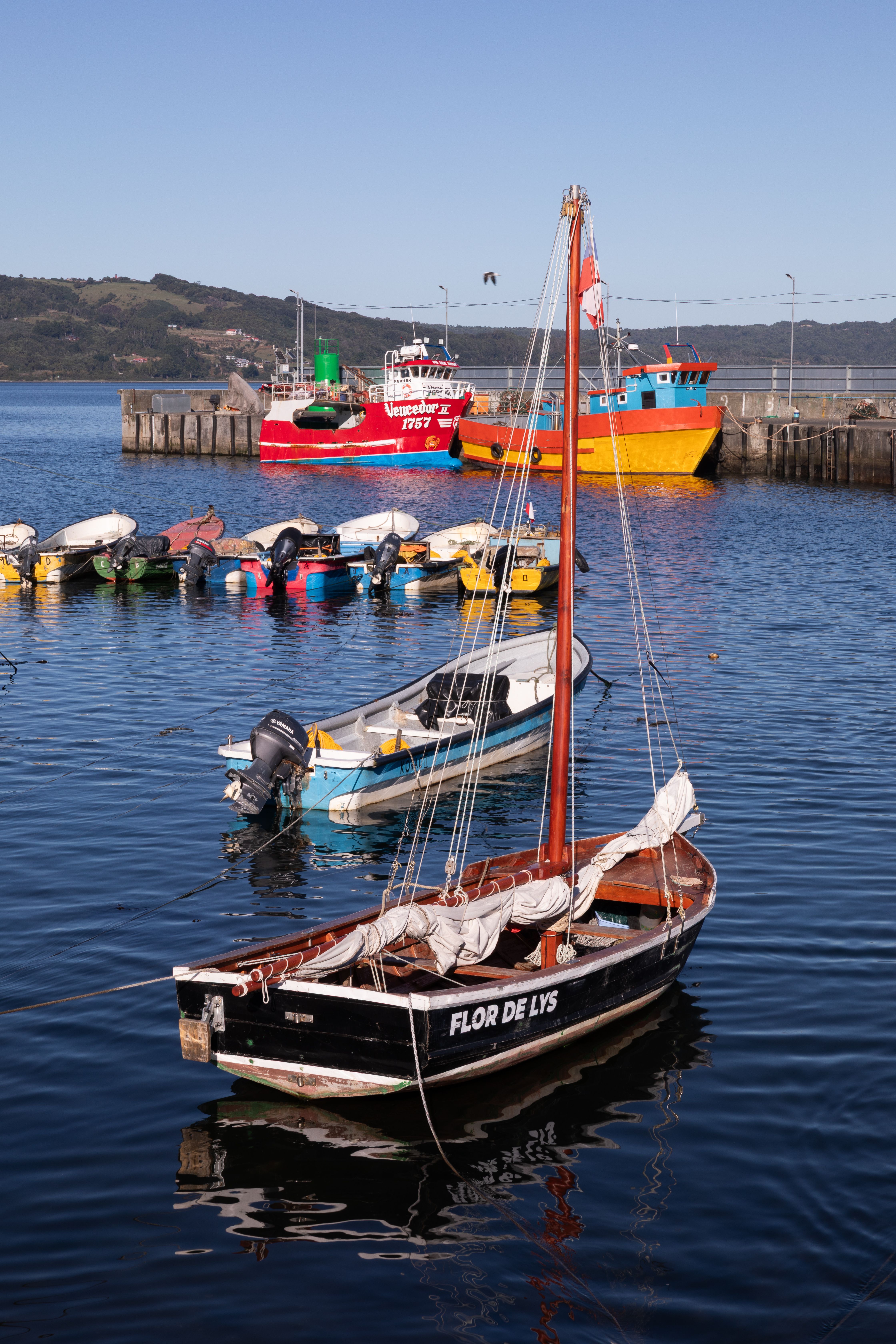 Fotomural Barcos de pesca vibrantes atracados en un puerto sereno en Los Lagos, Chile, con montañas de fondo.