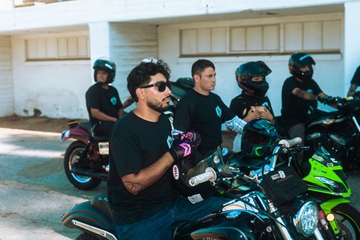 Motorcyclists gather outdoors, gearing up for a daytime ride with their bikes and helmets.