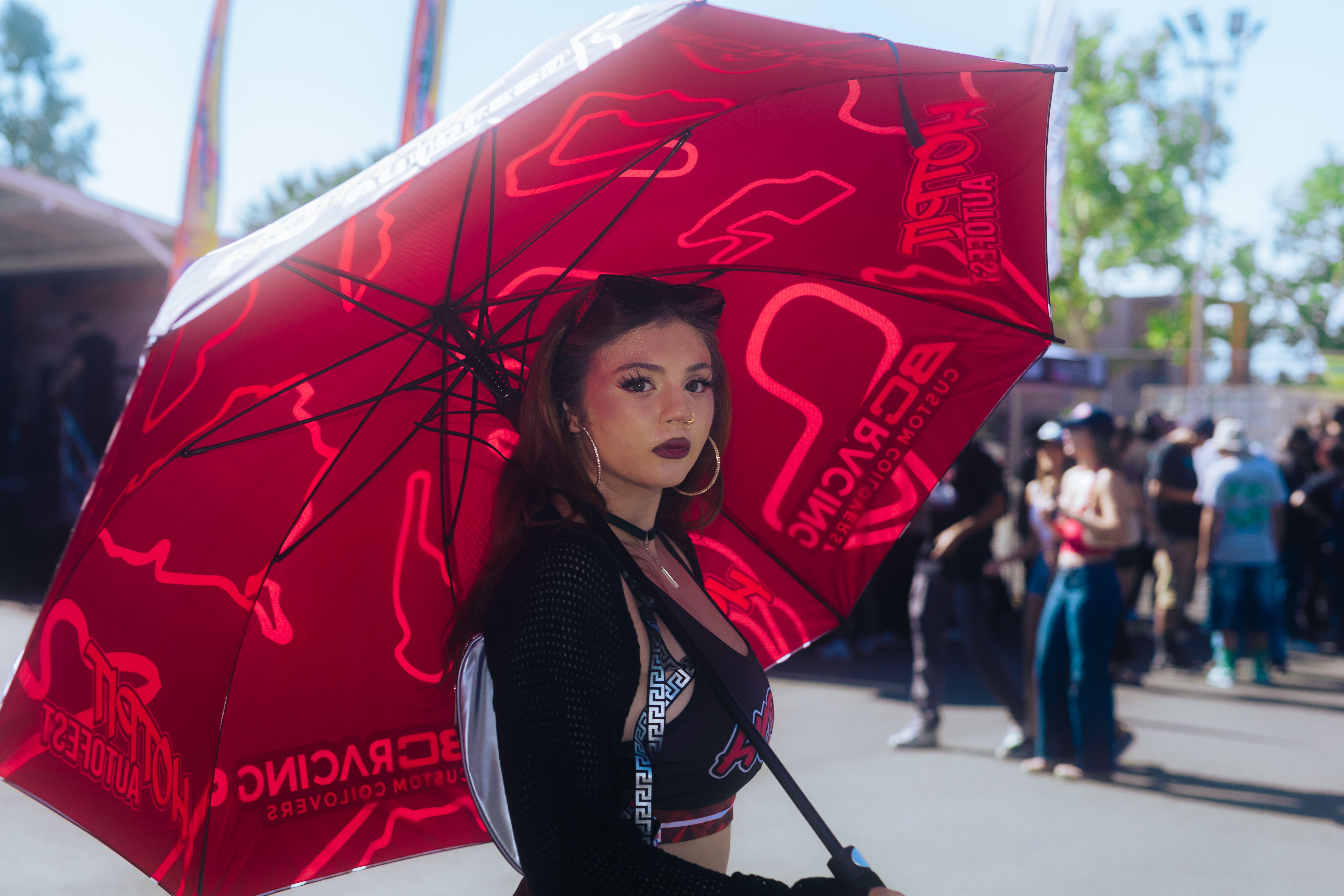 A fashionable woman with a red umbrella stands out at an outdoor event, creating a vibrant and lively scene.