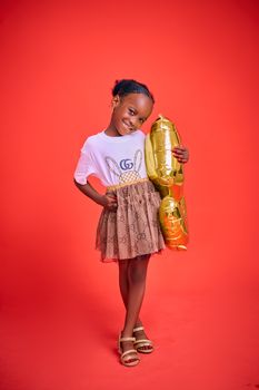 Happy child in festive outfit holding a gold balloon against a vibrant red backdrop.