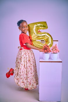 Cheerful girl celebrates birthday with a gold balloon and floral decor in a studio.