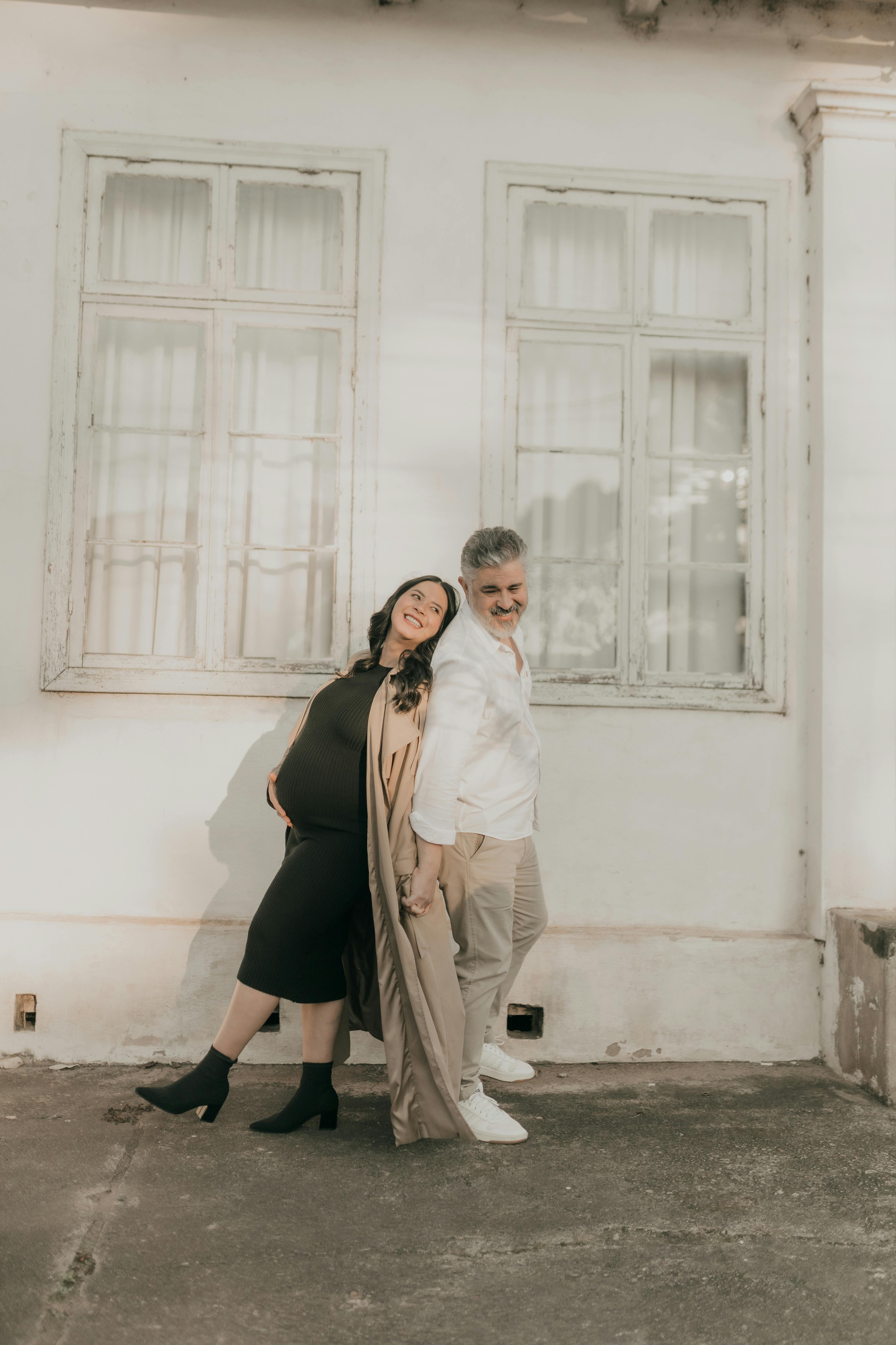 Smiling pregnant couple standing outside holding hands, embracing joy and anticipation.