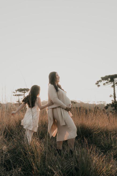 Free A mother with child walks in a sunlit field, capturing a serene family moment outdoors. Stock Photo