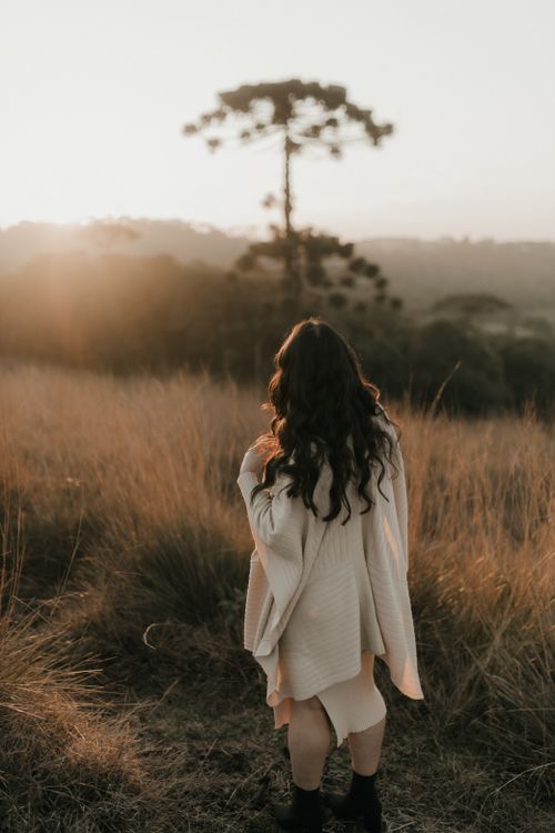 Free A woman enjoying the sunrise over a field, standing near a distinct tree silhouette. Stock Photo