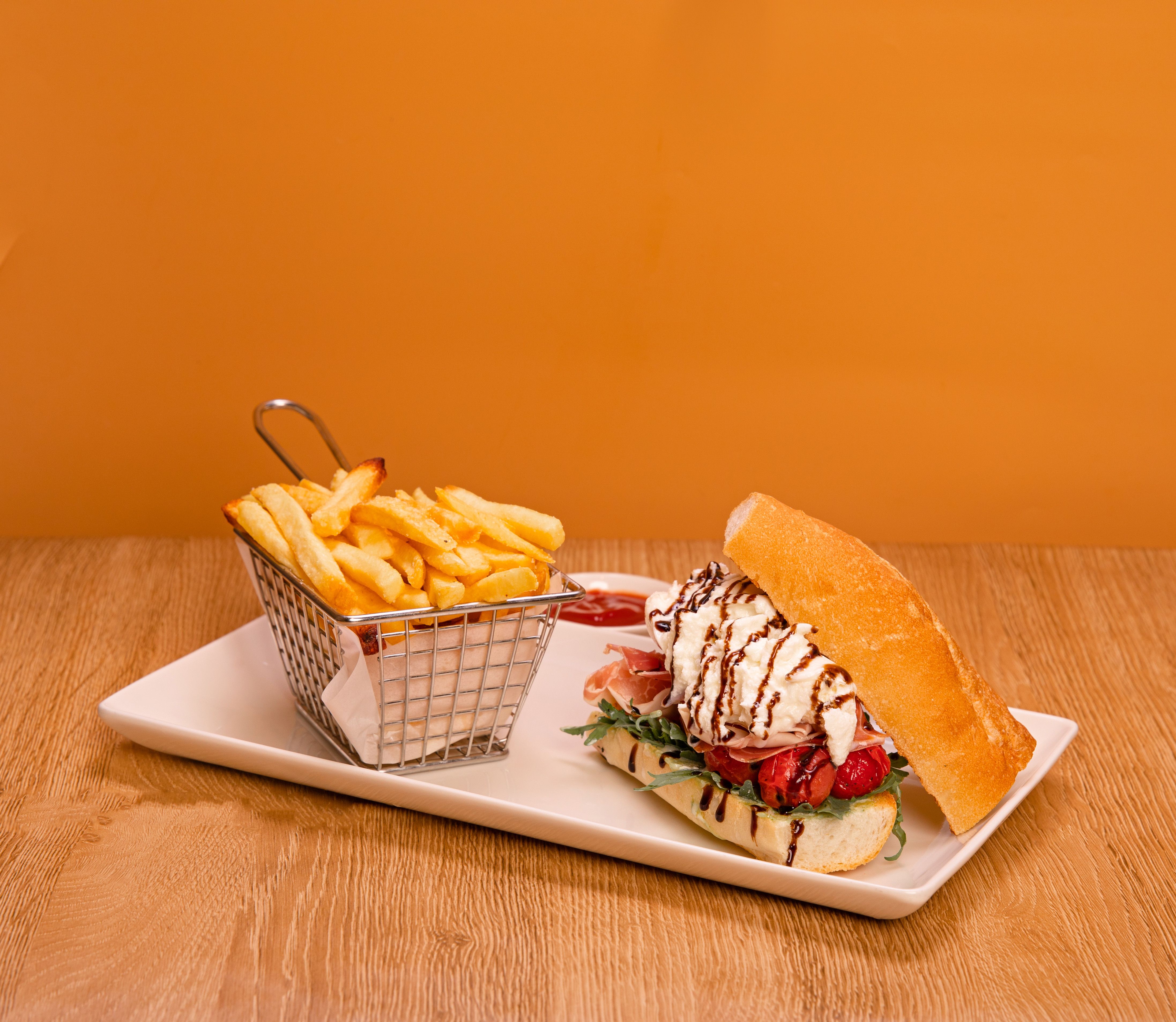 Free Delicious gourmet sandwich with fries served on a white plate against a warm orange background. Stock Photo