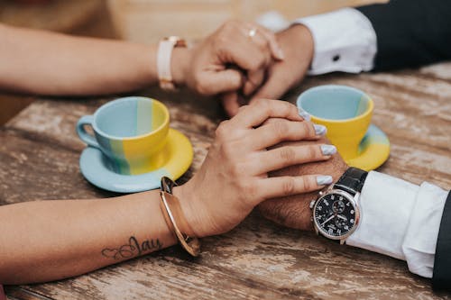 Couple Holding Each Others Hands With Ceramic Cups on the Table