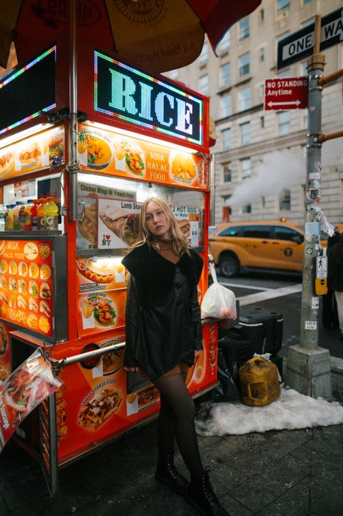Free A woman poses by a vibrant street food cart on a bustling city street. Stock Photo