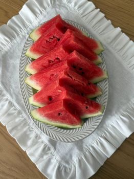 Juicy watermelon slices arranged on an elegant plate with a white cloth background.