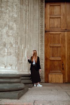 Fashionable woman poses beside a large ornate door with classic architecture.