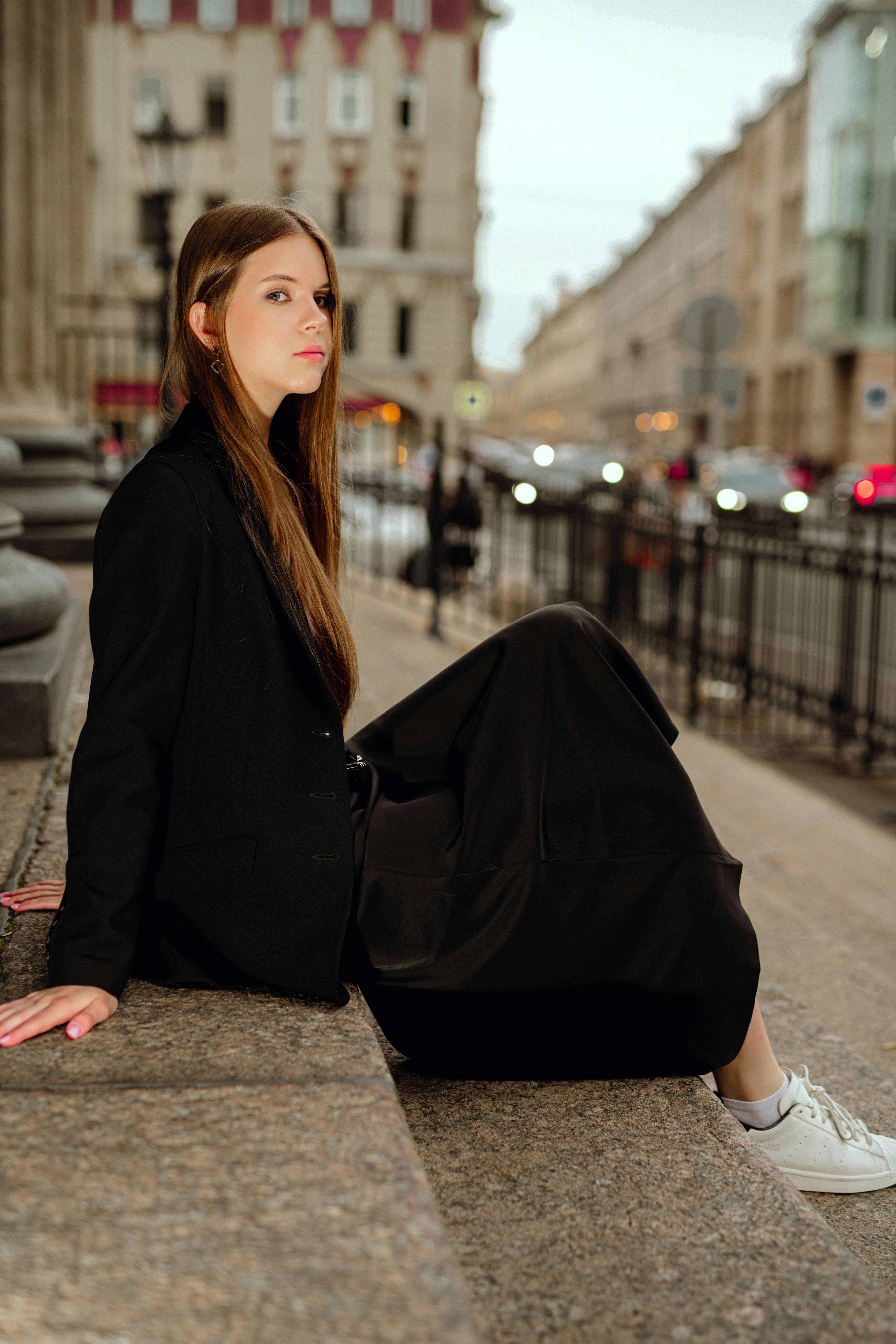 Stylish woman in black attire sitting on city steps with a thoughtful look. Urban casual fashion.