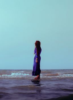 A young woman stands gracefully by the beach at twilight, creating a serene and contemplative scene.