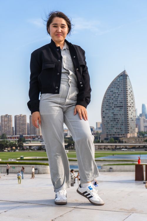 Free A young woman standing confidently outdoors with modern city architecture in the background. Stock Photo
