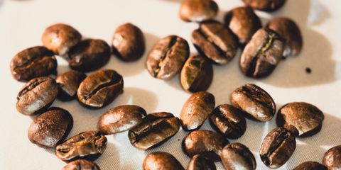 Bright close-up of roasted coffee beans scattered on white surface, ideal for coffee-themed designs.