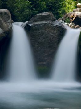A tranquil scene of twin waterfalls cascading in a lush, green forest during the day.