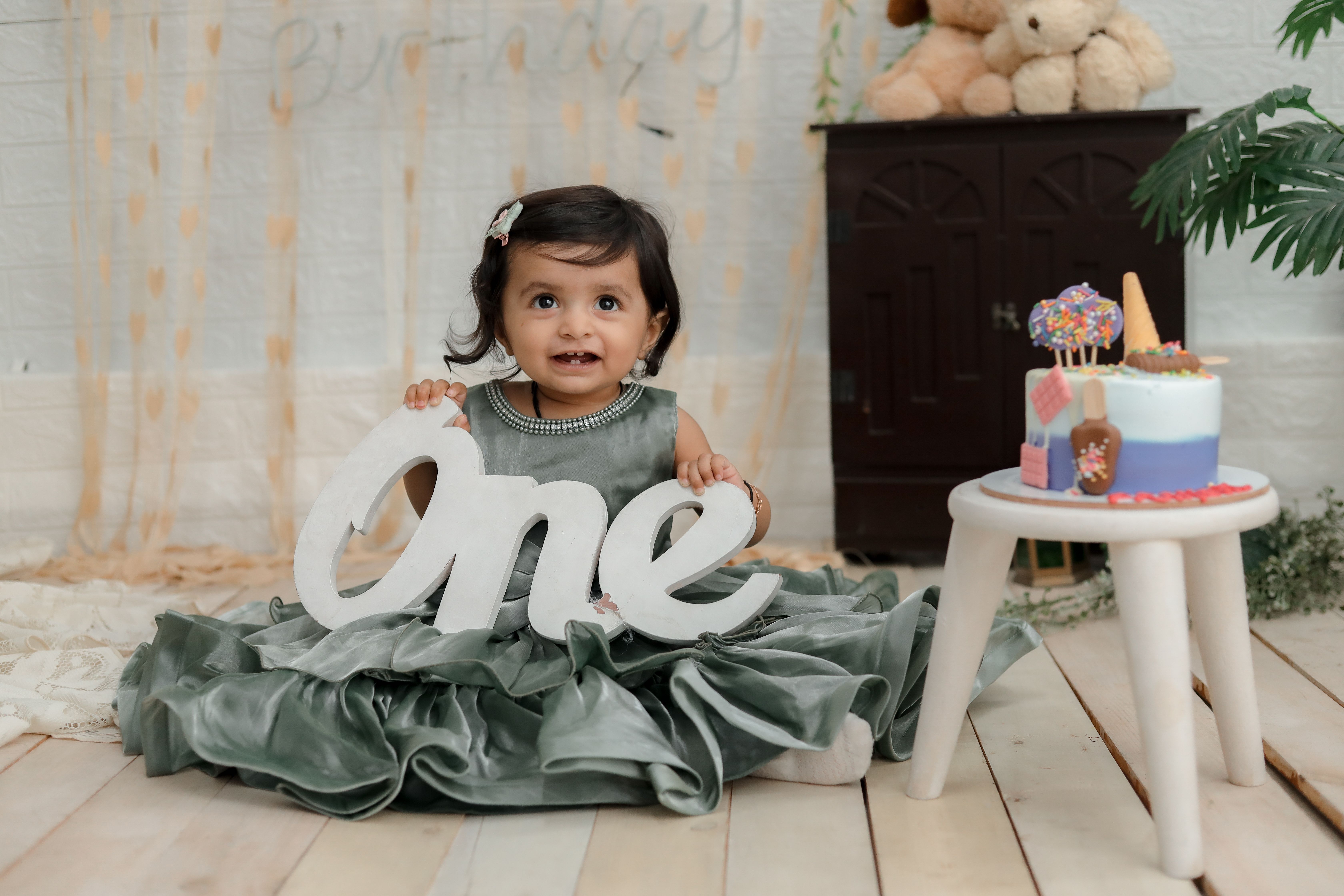 A cute baby girl celebrating her first birthday in an elegant green dress with a cake and decor.
