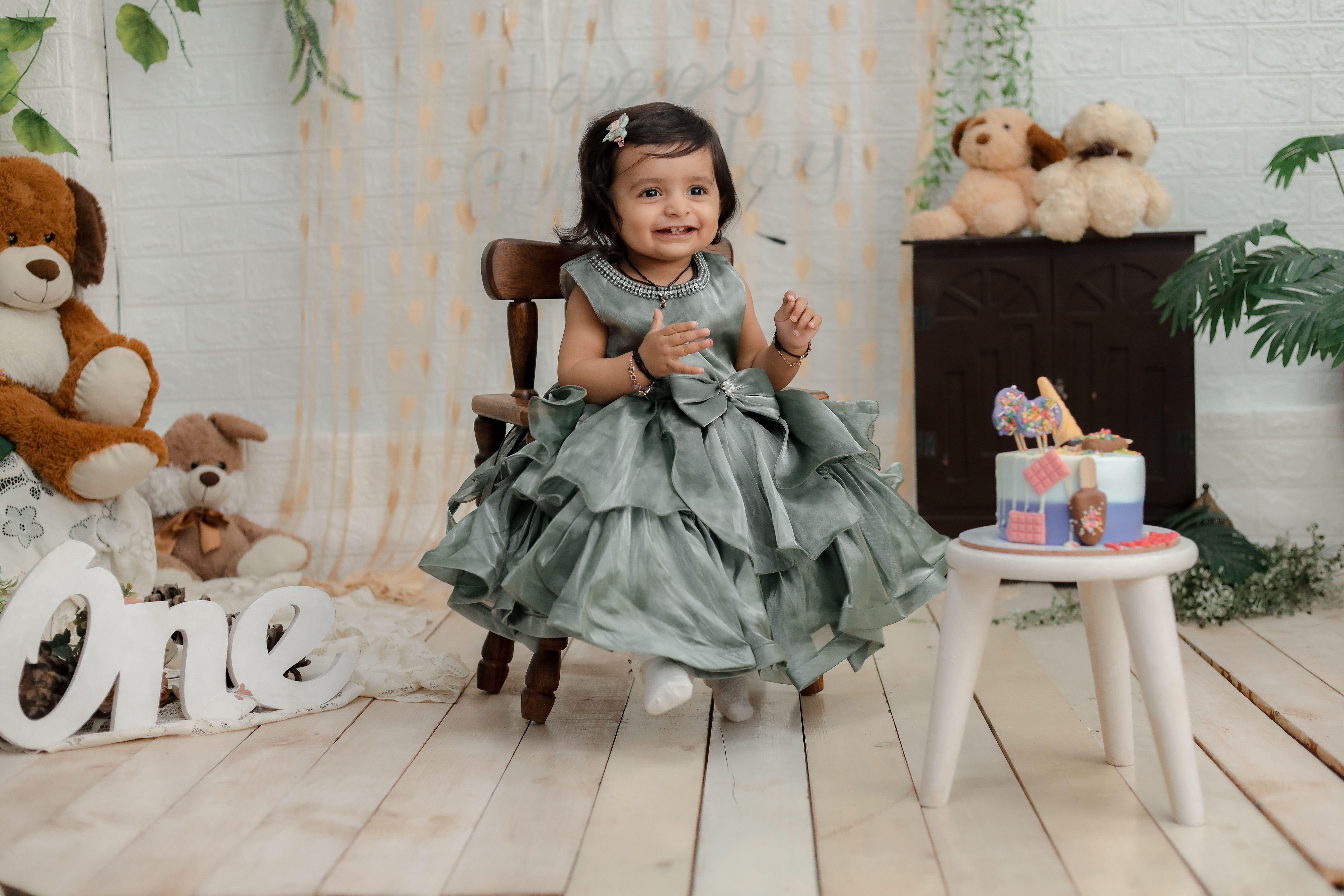Adorable baby in overalls sitting on a blanket outdoors, smiling brightly.