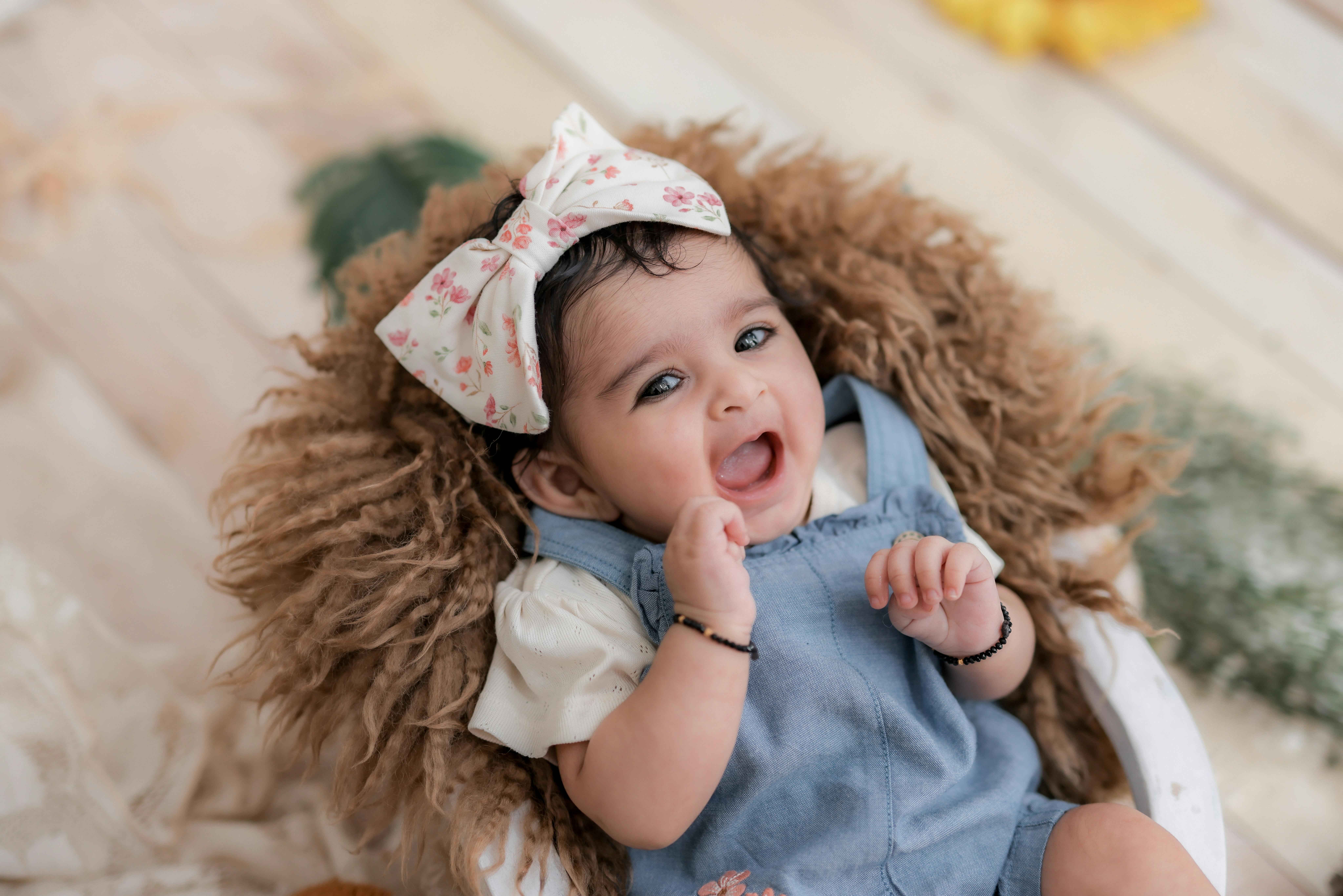 Charming baby with a floral headband smiling joyfully while lying down.