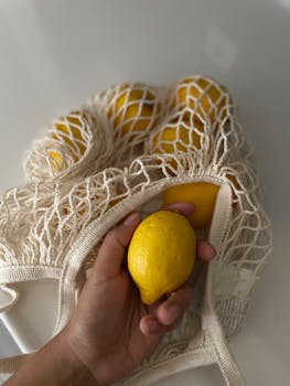 Close-up of hand holding lemon in eco-friendly mesh bag, promoting sustainability.