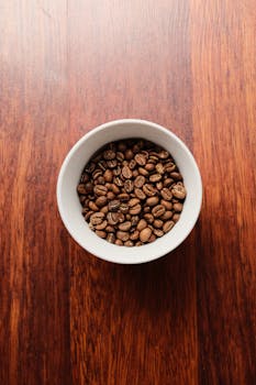 Top view of a bowl filled with coffee beans on a rustic wooden table.