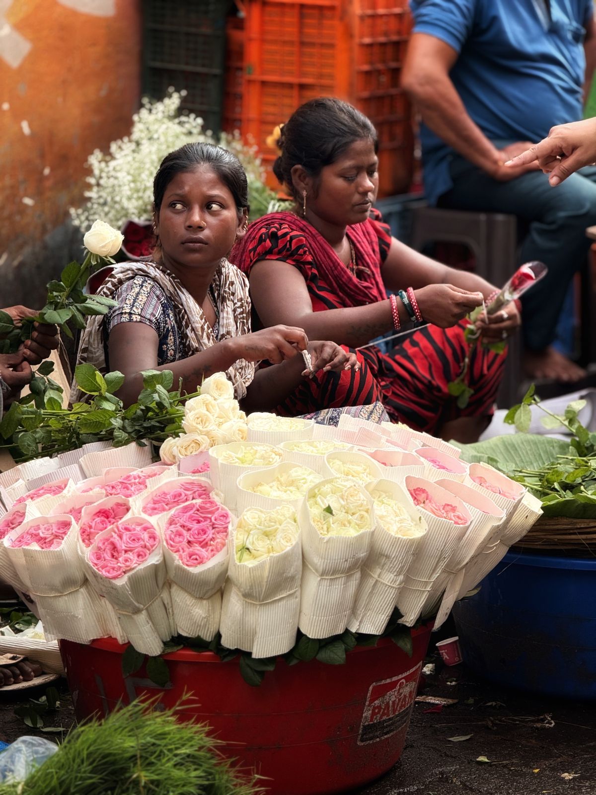 Two vendors at a vibrant flower market surrounded by colourful roses and blooms