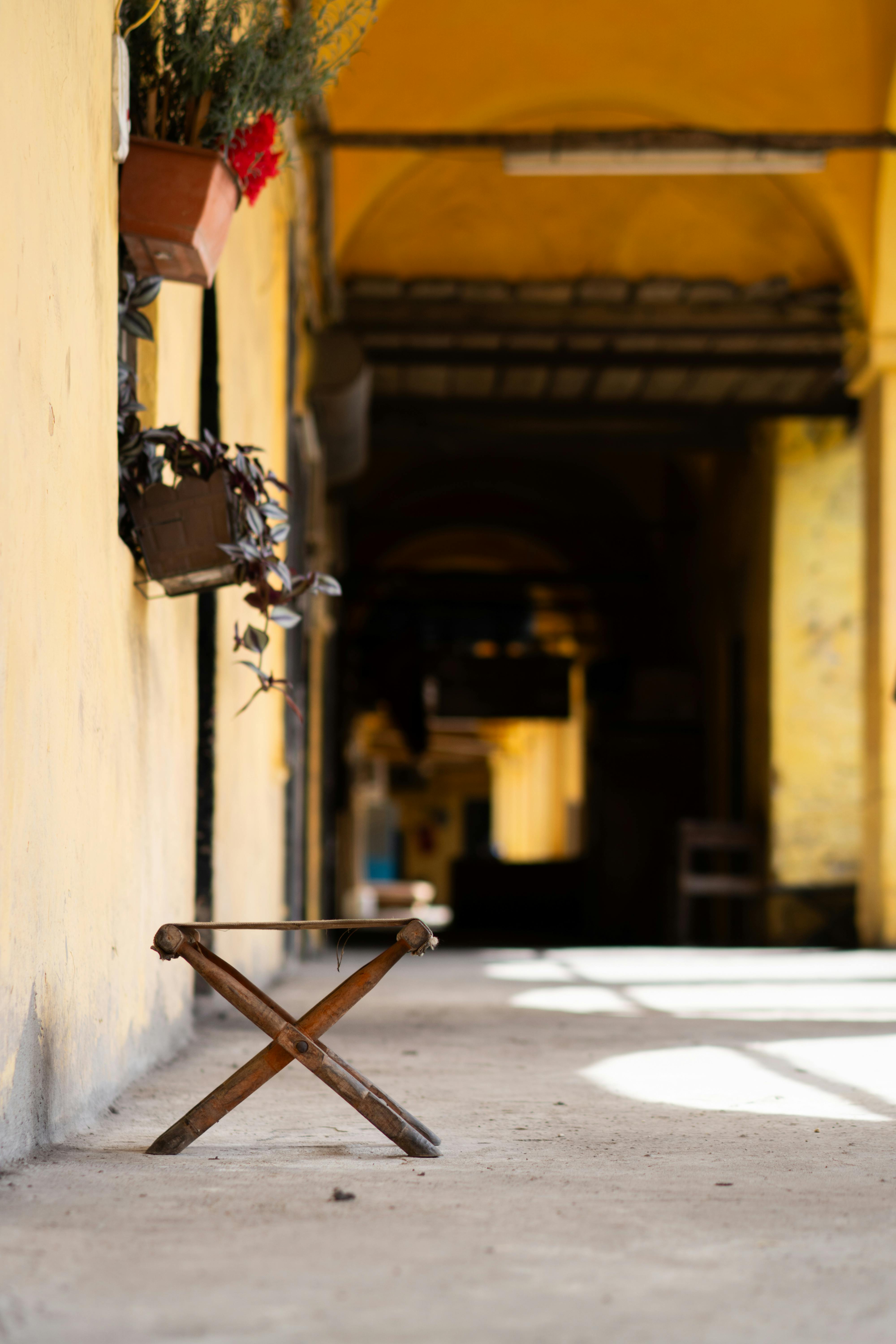 Gratuit Un scaun solitar din lemn într-un coridor însorit și plin de umbră, cu plante în ghiveci viu colorate. Fotografie de stoc