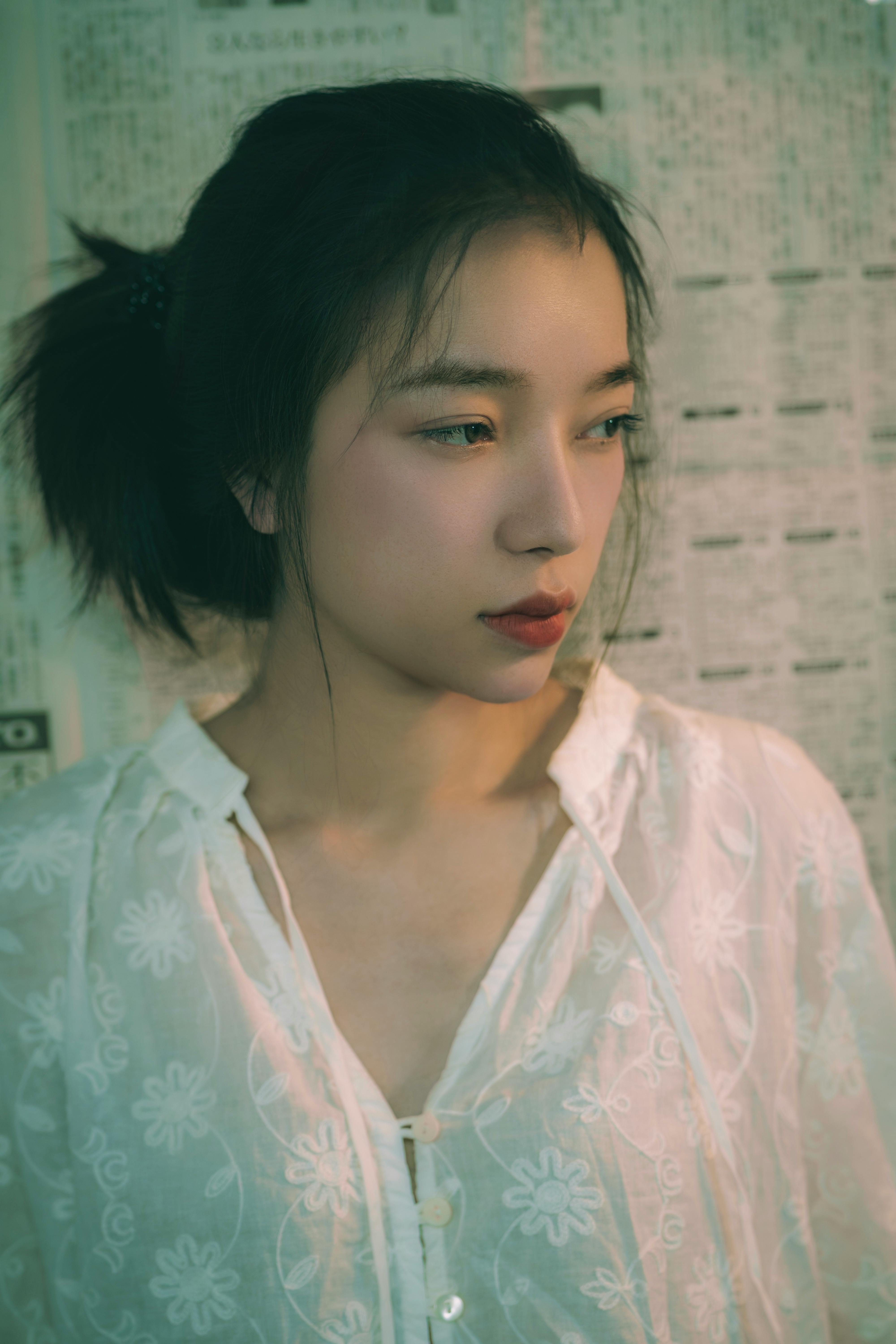 Portrait of a woman in a white dress against a newspaper wall, soft lighting.
