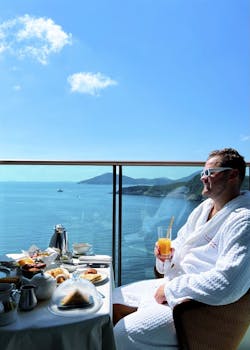 Man in a bathrobe enjoying breakfast on a balcony overlooking the ocean in Hong Kong.
