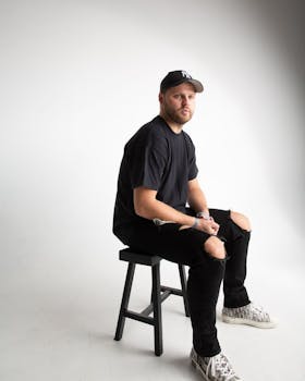 Studio portrait of a seated man wearing casual black outfit and sneakers.